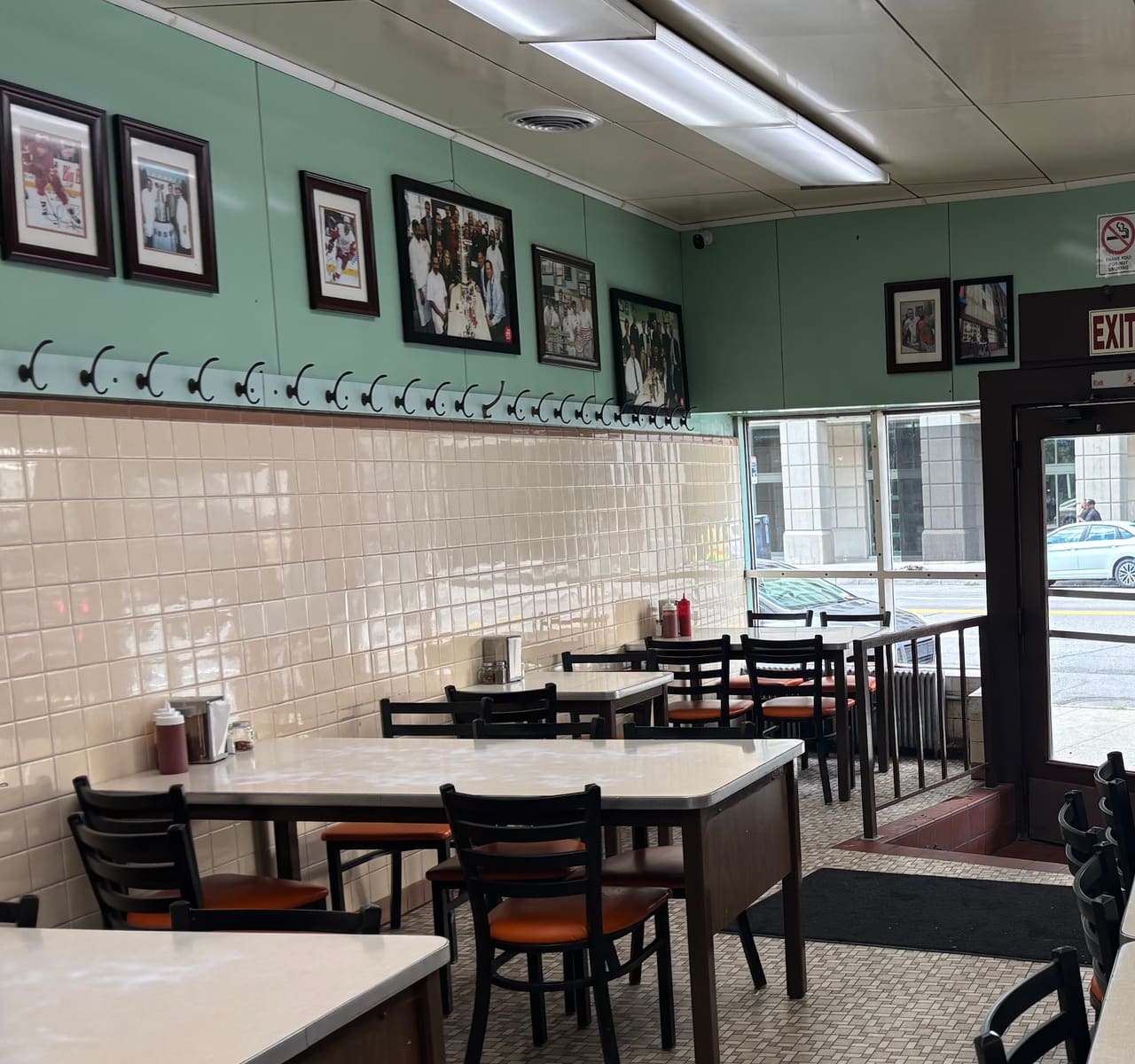 The dining room at Lafayette Coney Island: mint green walls, cream subway tile, a rail of coat hooks and framed black-and-white photographs above laminate tables.