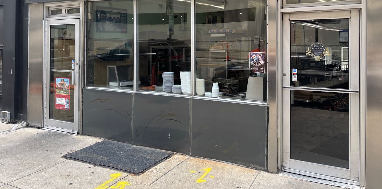 The stainless steel and glass storefront of Lafayette Coney Island at number 118, with stacked cups in the window.
