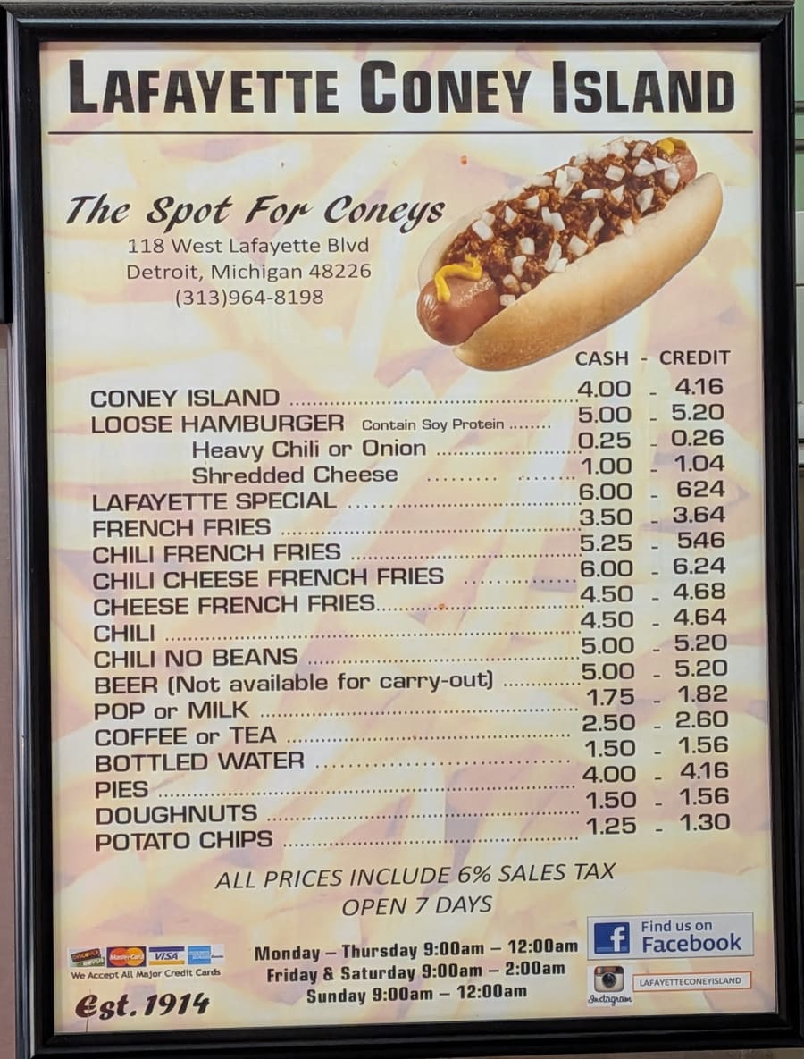 The framed printed menu board above the counter at Lafayette Coney Island, headed “The Spot For Coneys”, listing coneys, loose hamburgers, fries and chili with separate cash and credit prices.