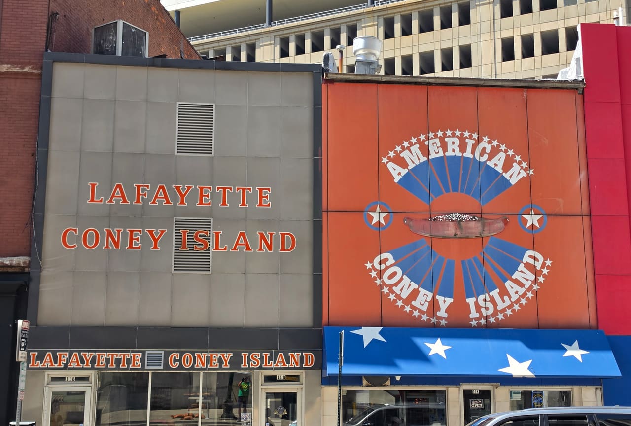 Lafayette Coney Island’s grey enamel frontage beside American Coney Island’s orange and blue painted facade on West Lafayette Blvd.